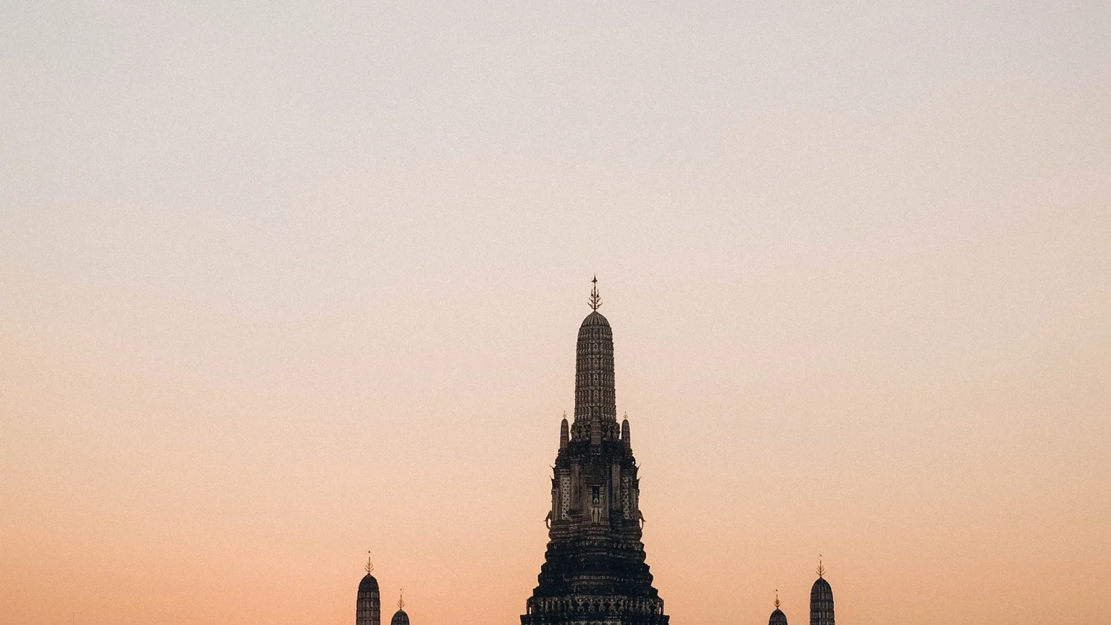 Grand Palace gilded spires and temple roofs along the Chao Phraya riverfront at golden hour