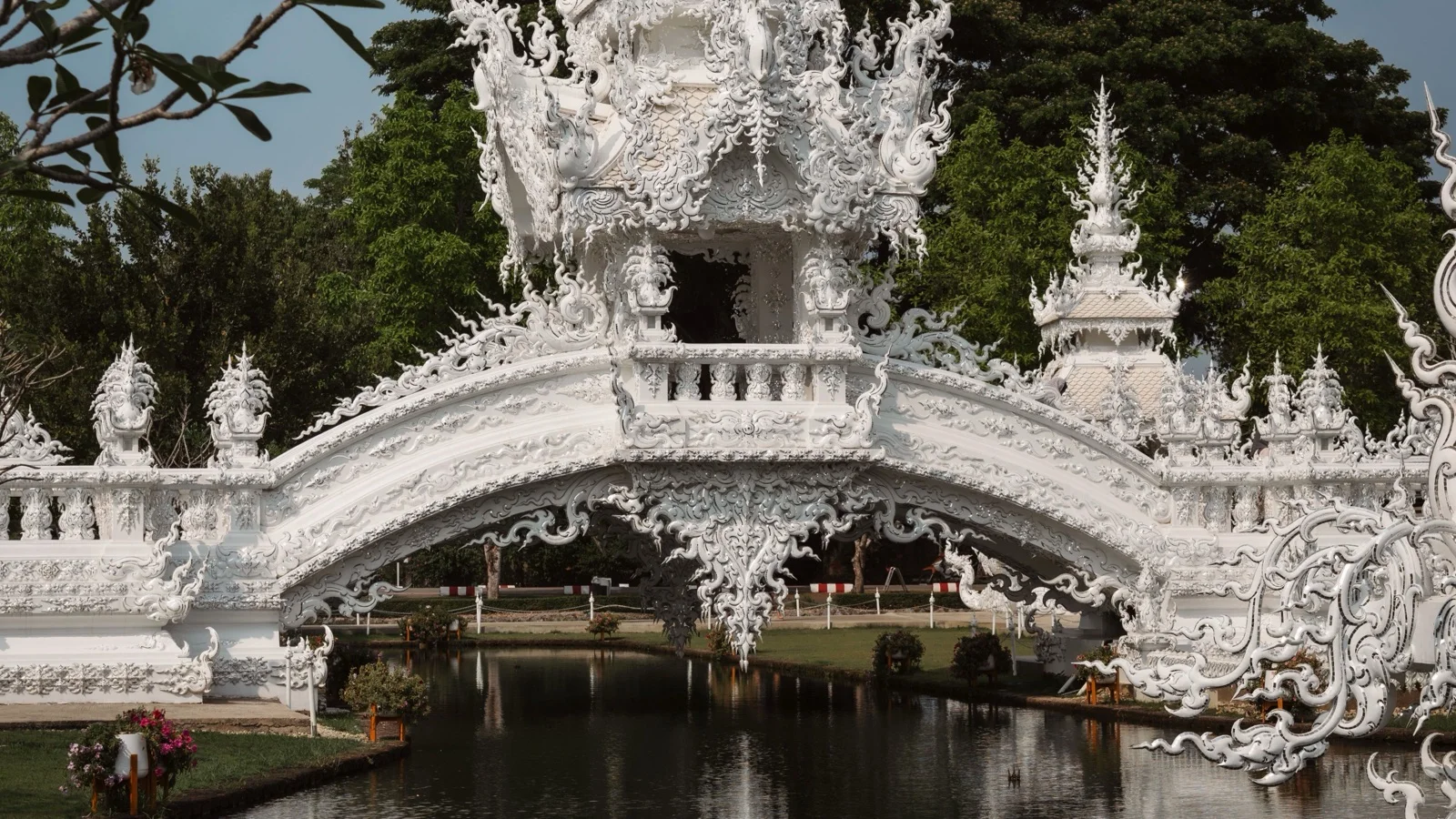 Mirrored white facade and bridge of Wat Rong Khun, the White Temple of Chiang Rai, glittering under a clear winter sky