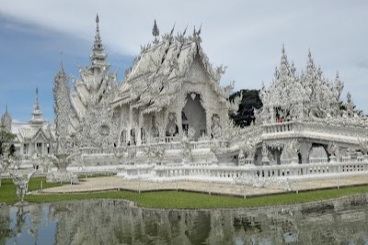 Mirrored all-white facade of Wat Rong Khun, the White Temple of Chiang Rai, under a clear morning sky