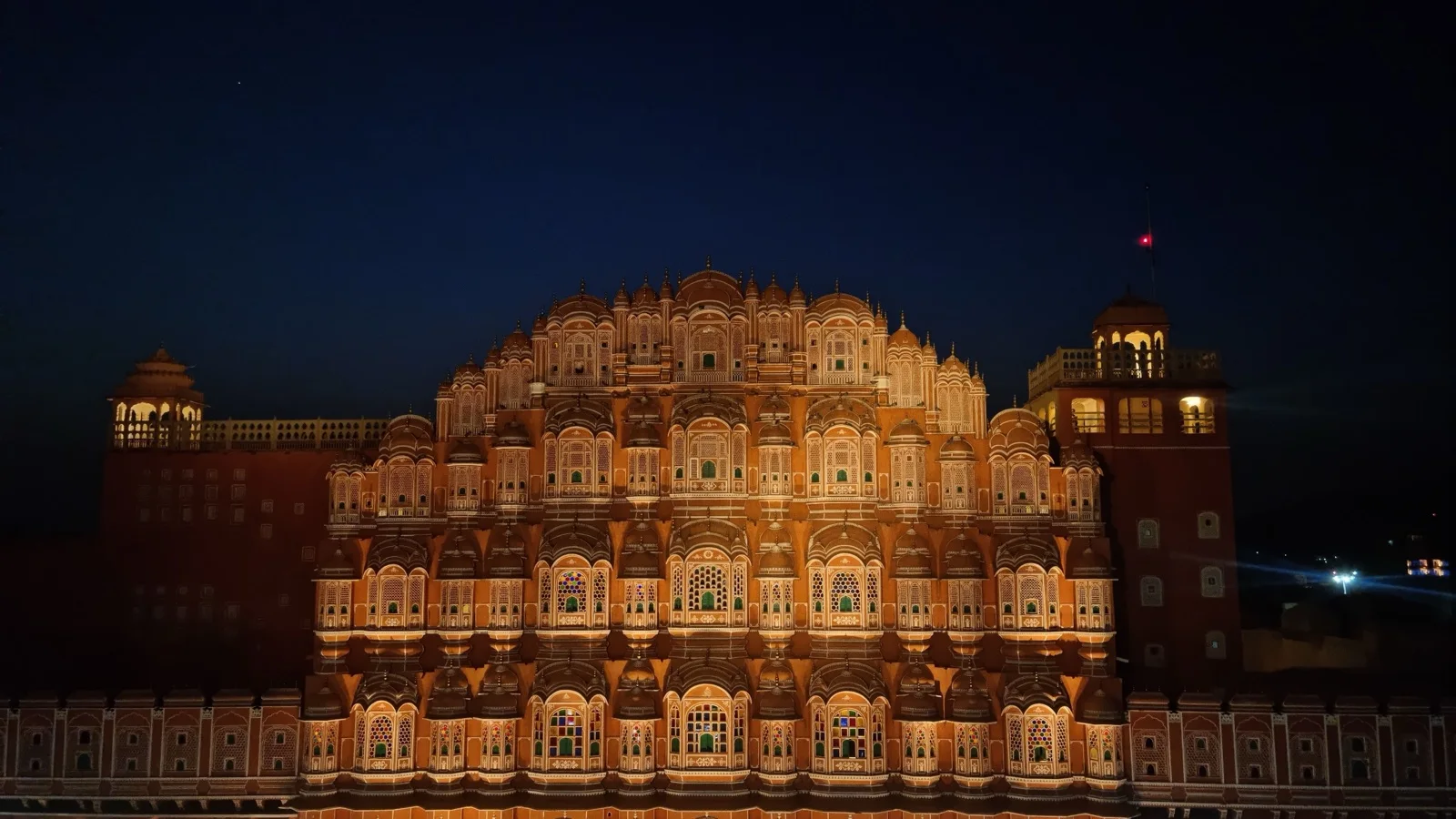 The pink sandstone facade of Hawa Mahal glowing at sunrise above Jaipur's old bazaar lanes