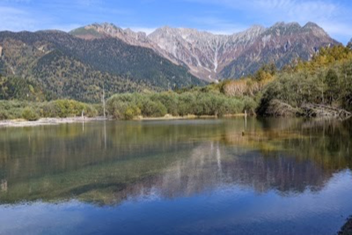 Taisho Pond dead trees reflected in clear alpine water with mountains in the background