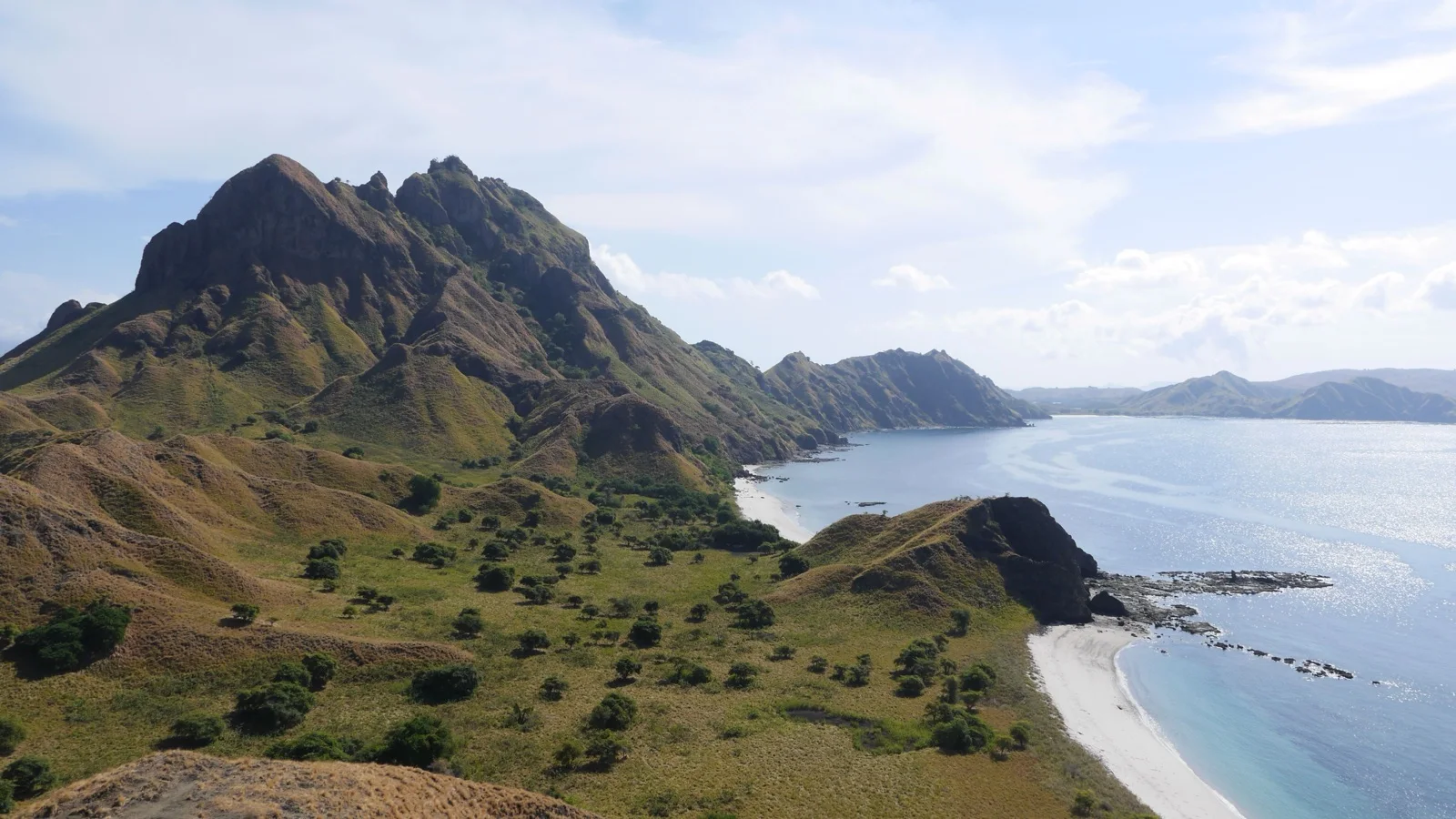 Sunrise over Padar Island's three bays, where savanna ridges divide pink, white, and grey sand beaches in Komodo National Park
