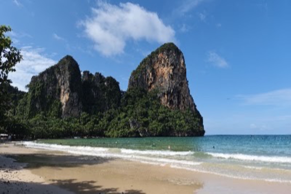 Longtail boats on turquoise water beneath towering limestone cliffs at Railay West Beach