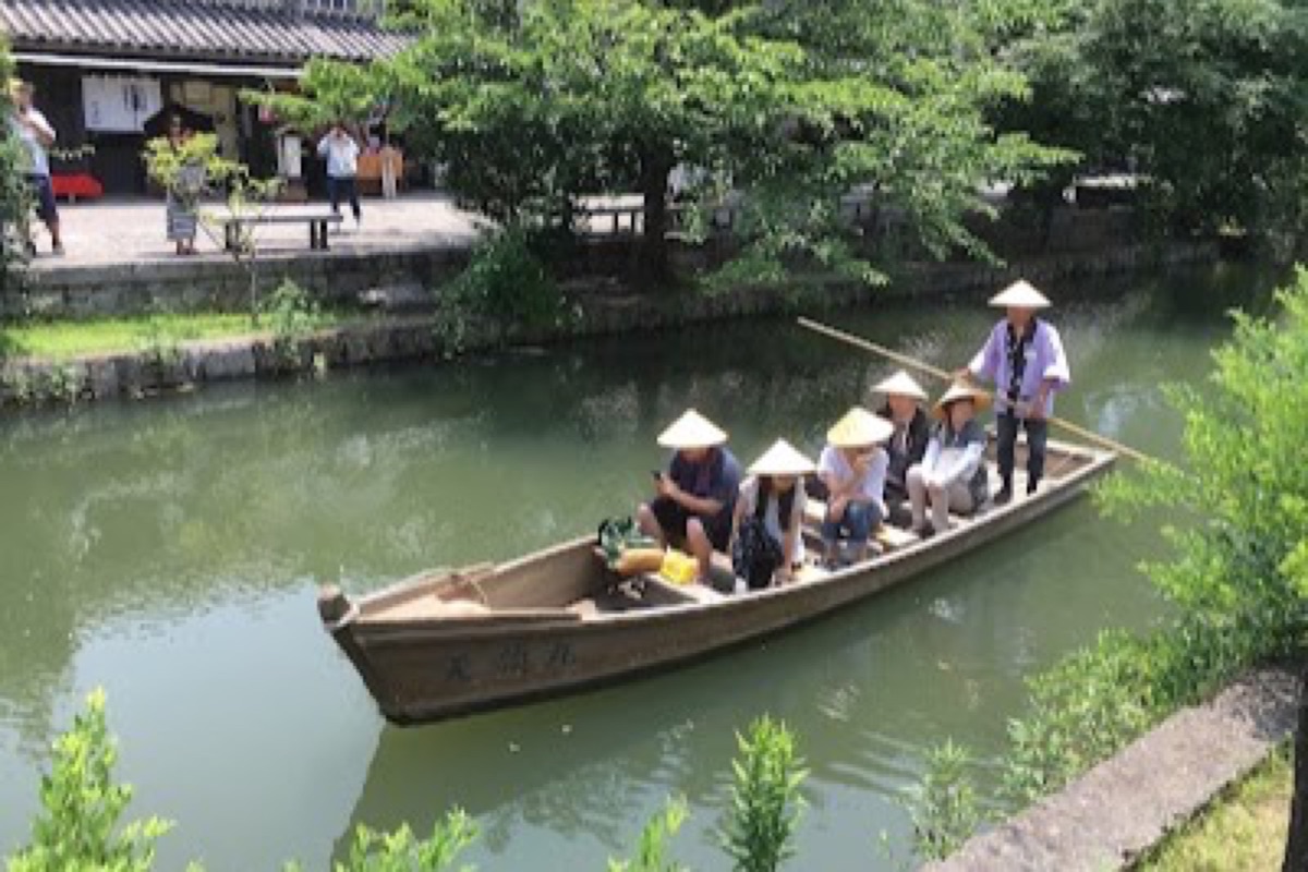 Traditional punting boat gliding under stone bridges on the Kurashiki canal with willow canopy