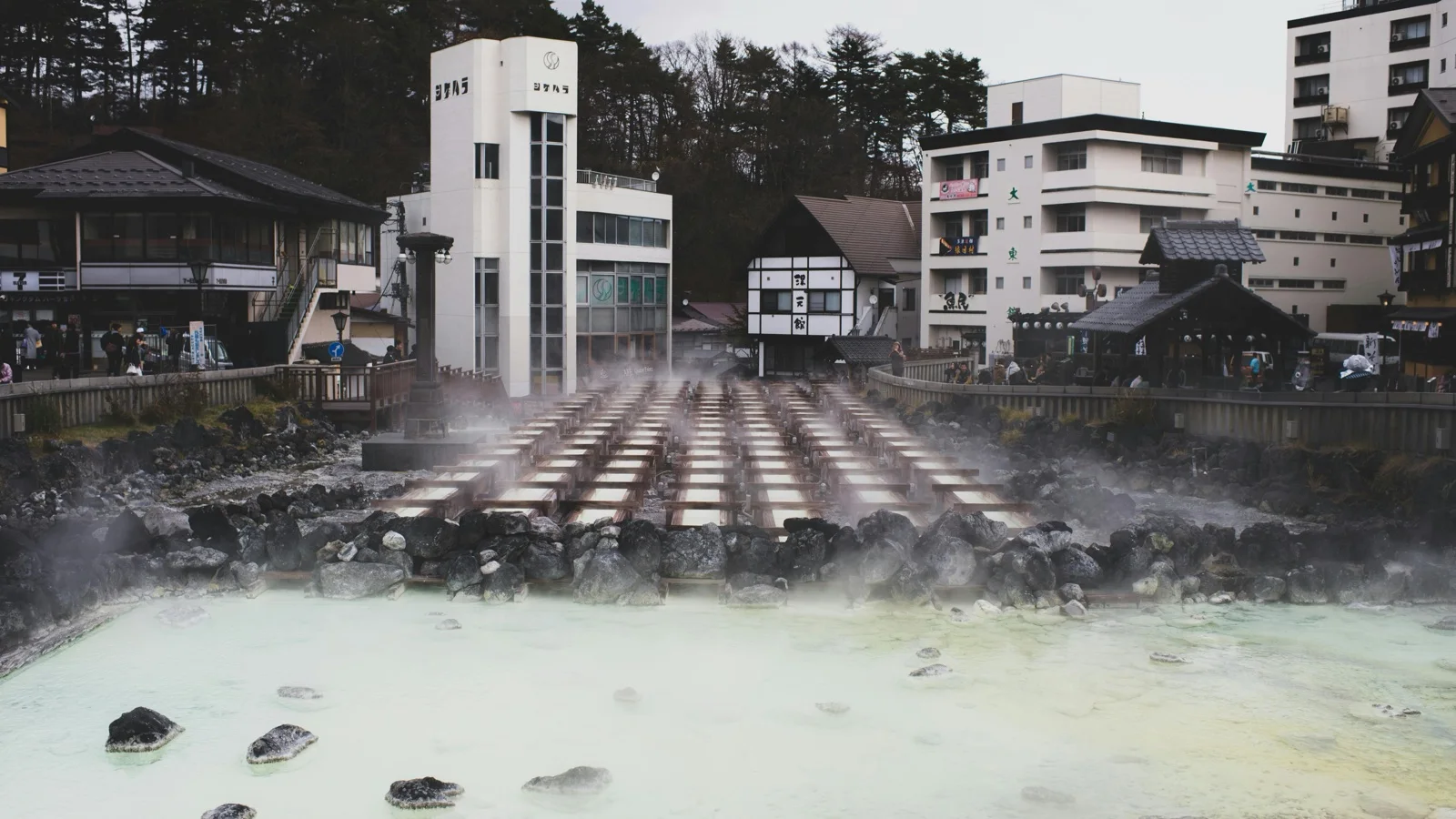Steaming Yubatake hot-water field with timber troughs at the center of Kusatsu Onsen at dusk