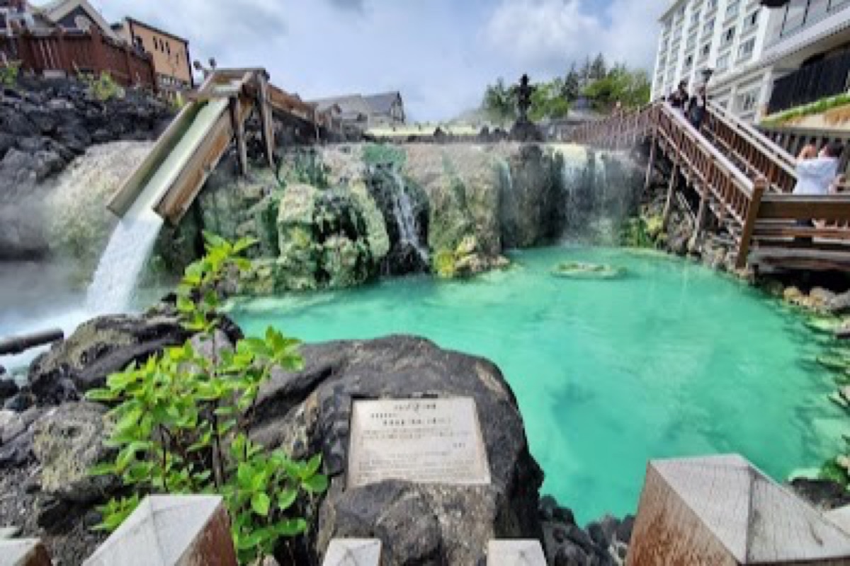 Yubatake hot-water field with steaming timber troughs lit up at night in Kusatsu Onsen