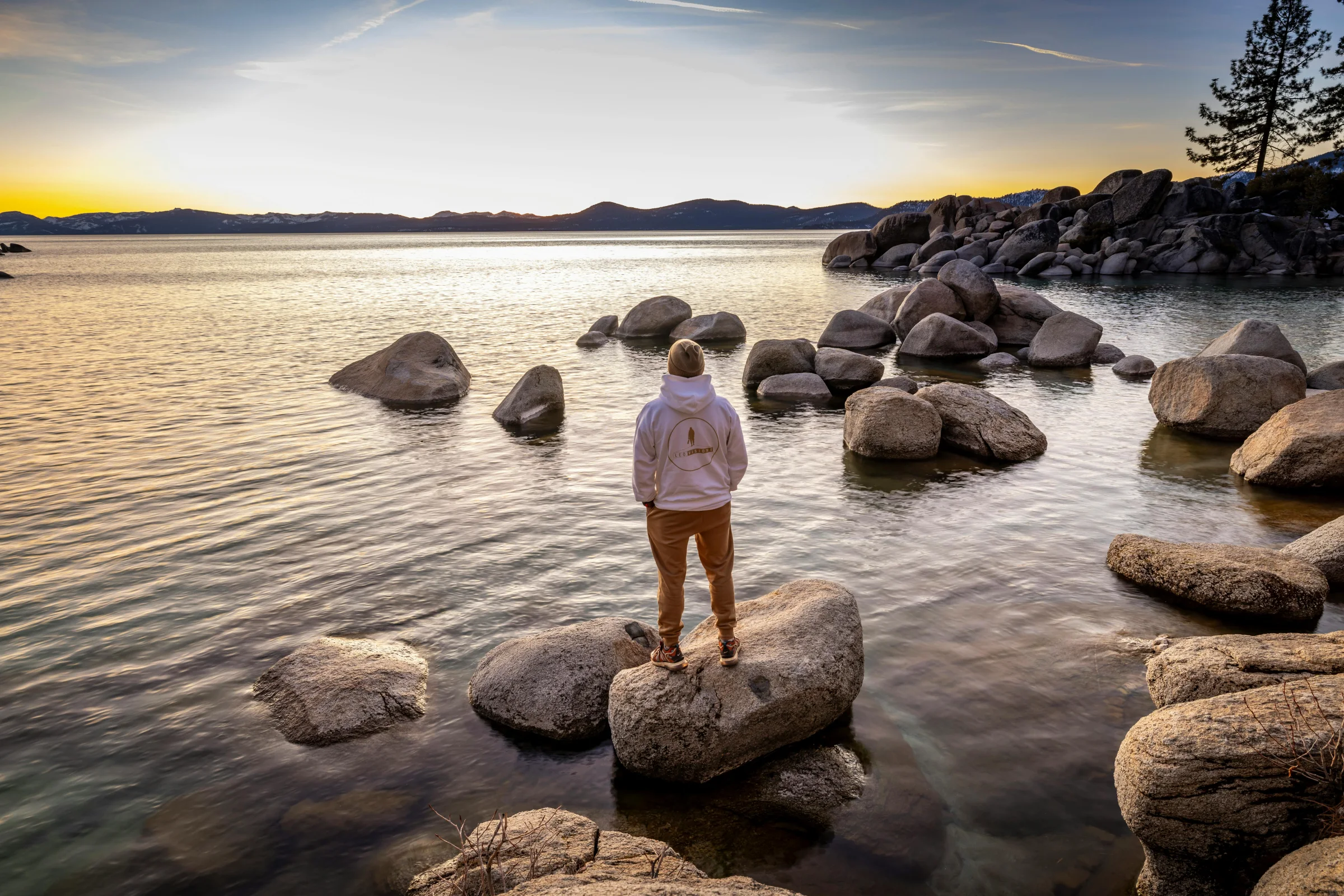 A wide sunrise view over Emerald Bay at Lake Tahoe with clear blue water and surrounding pine-covered mountains.