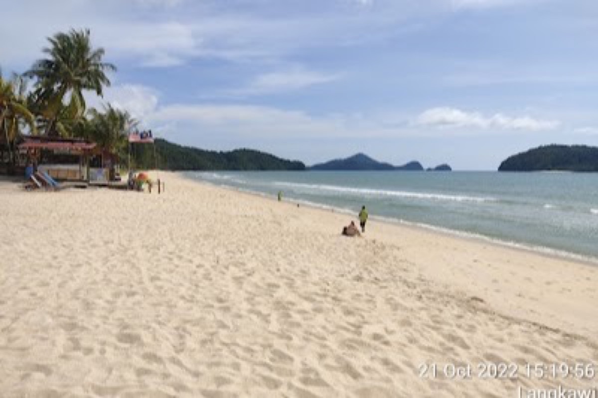 Pantai Cenang beach strip with sunbeds, palm trees, and calm water at golden hour