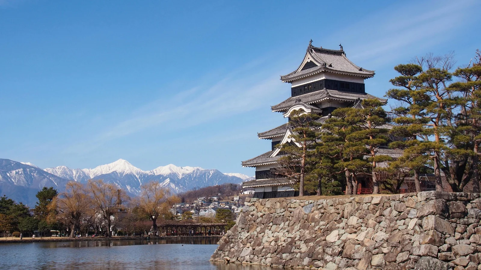 Matsumoto Castle's black exterior reflected in the moat with cherry-blossom trees in the foreground