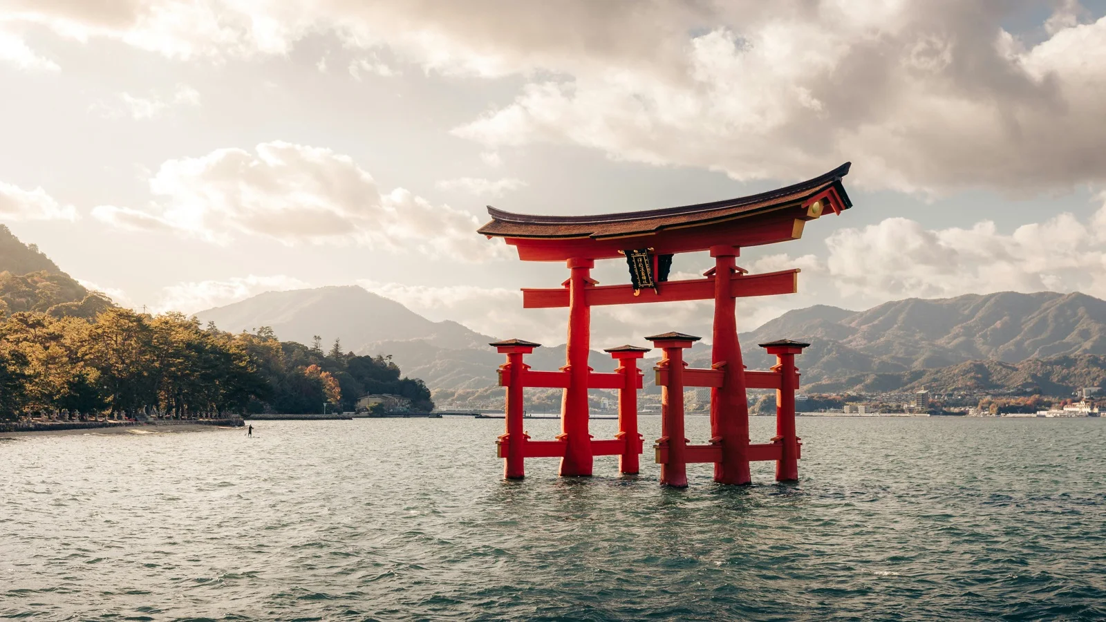 The vermilion O-Torii Gate standing in Hiroshima Bay shallows at low tide with Itsukushima Shrine beyond