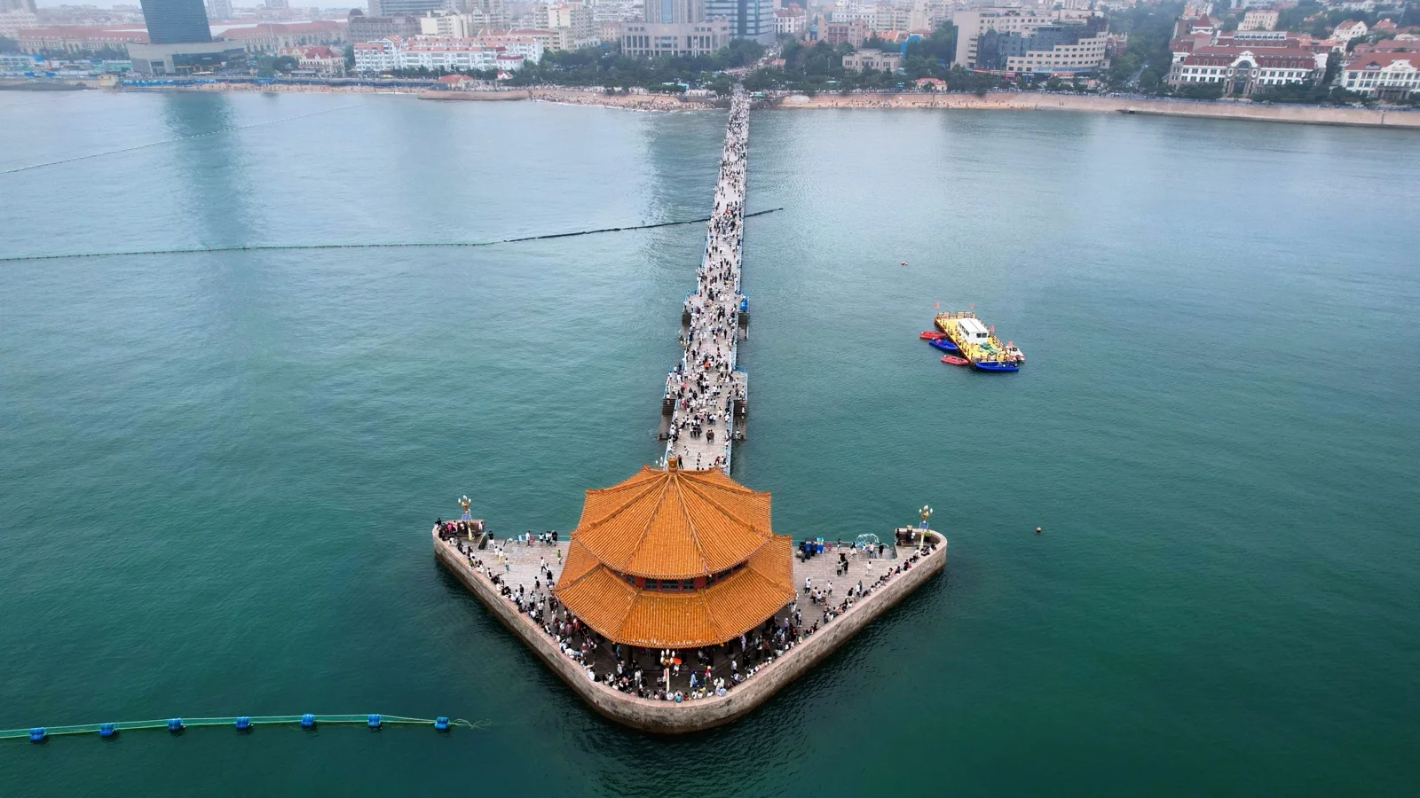 Golden hour view of Zhanqiao Pier and the Huilan Pavilion in Qingdao, China, with the old town coastline beyond