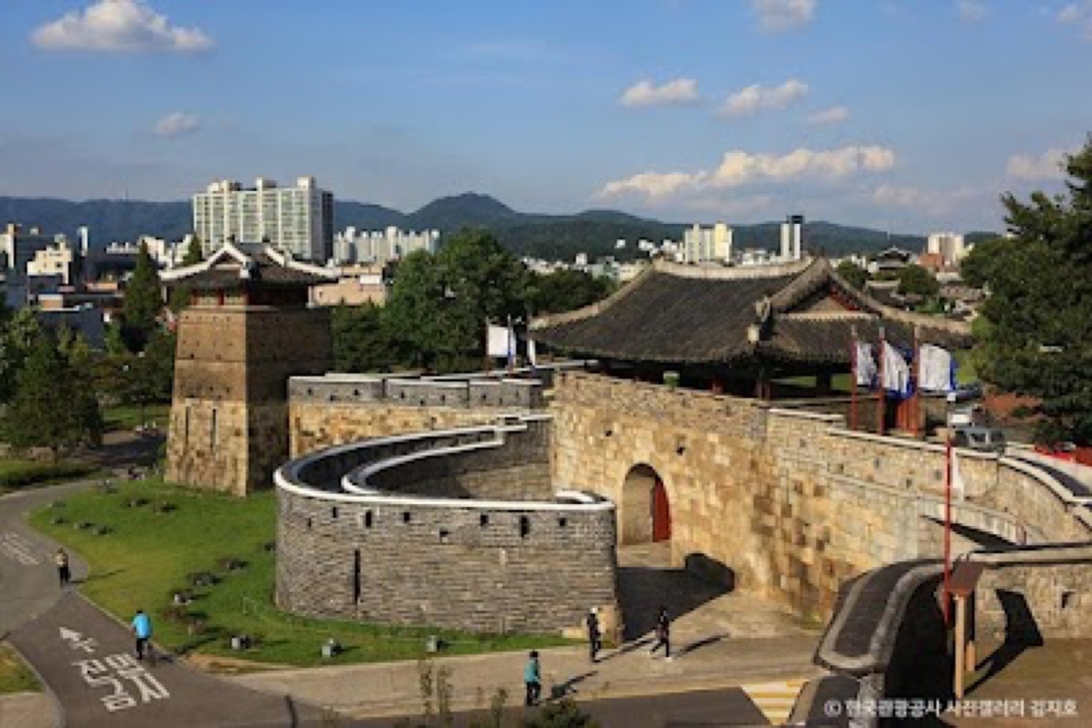 Hwaseong Fortress stone ramparts and pavilions with spring cherry blossoms along the UNESCO wall in Suwon