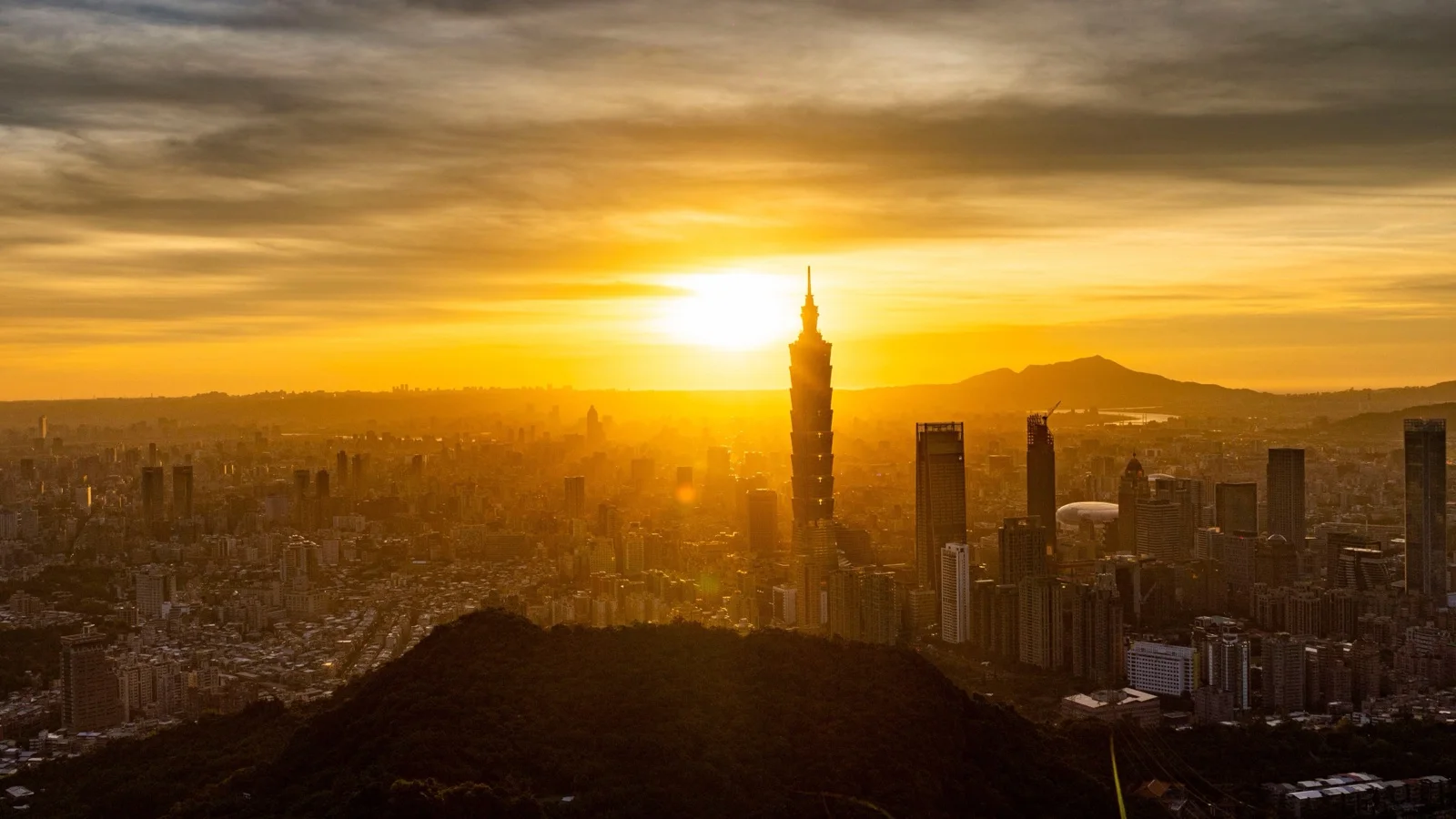 Taipei 101 above the Xinyi skyline with mountains behind on a clear spring evening