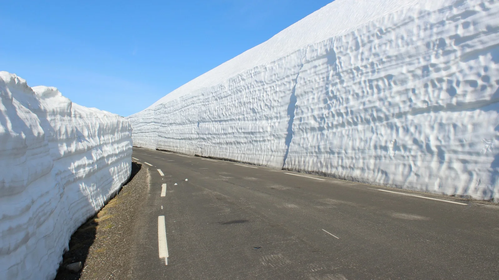 Towering snow corridor walls along the Tateyama Kurobe Alpine Route with alpine peaks visible above the carved road