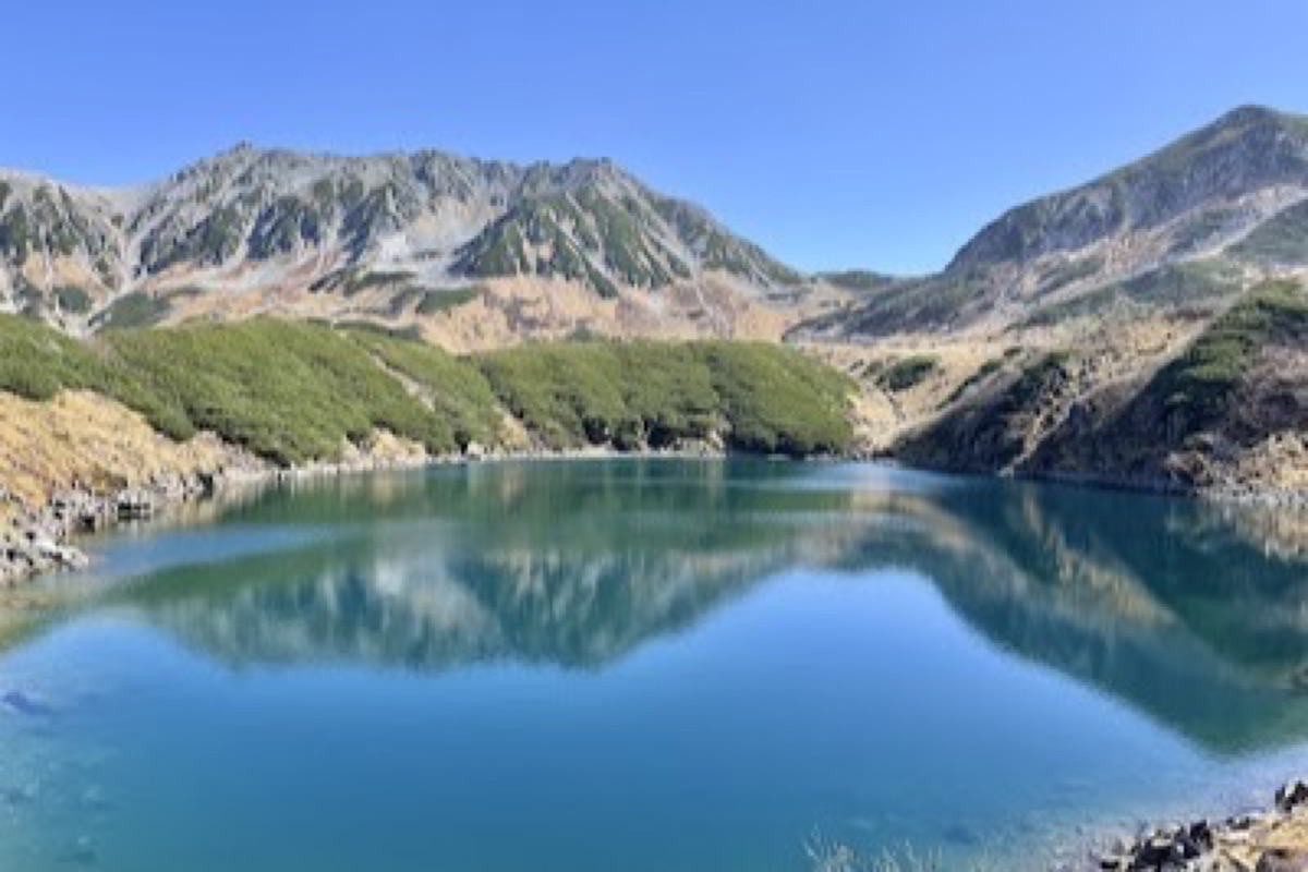 Mikurigaike volcanic crater pond reflecting Tateyama peaks on a clear spring morning