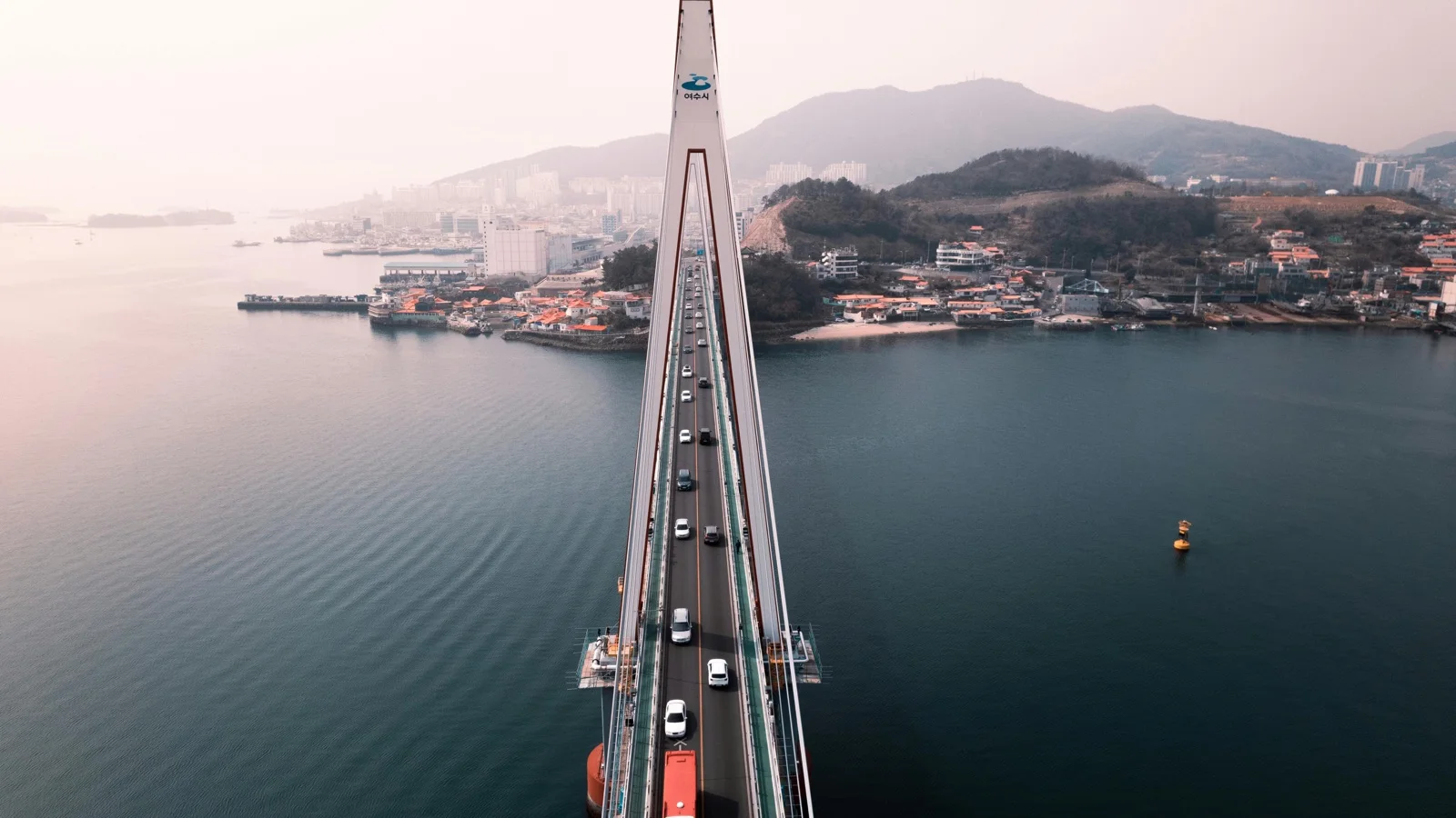 Yeosu harbor waterfront with Odongdo Island lighthouse and coastal mountains in soft evening light