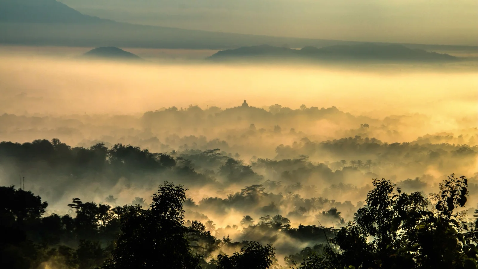 Dawn mist settling over Borobudur's stupas with Mount Merapi rising on the horizon